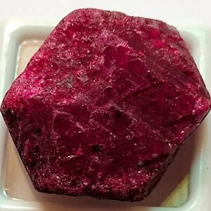 May include: A large, deep red ruby gemstone with a hexagonal shape and a rough, natural surface.