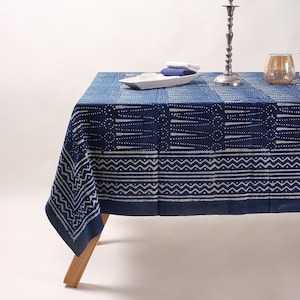 May include: A blue and white patterned tablecloth with a geometric design. The tablecloth is laid out on a table with a silver candlestick and a glass candle holder.