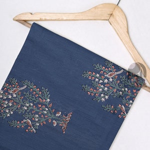 May include: A blue cotton fabric with a white and green floral pattern and small pink birds. The fabric is hanging on a wooden hanger.