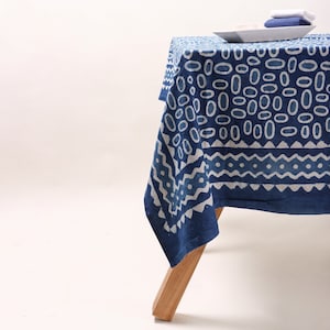 以下が含まれることがあります： 幾何学模様の青と白のテーブルクロス。テーブルクロスは木製のテーブルにかけられています。