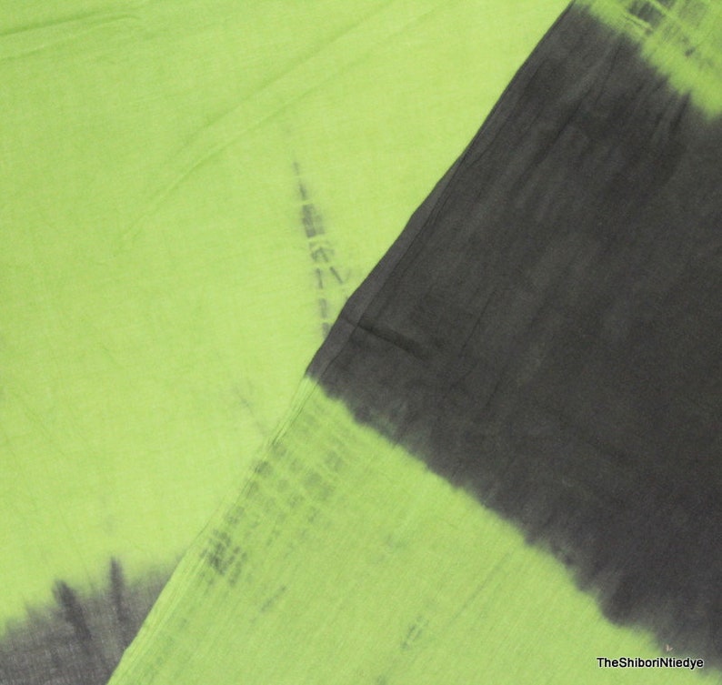 Op de afbeelding: Een groene en zwarte tie-dye stof met een verloop effect. De stof is zacht en licht, waardoor het perfect is voor een verscheidenheid aan projecten.