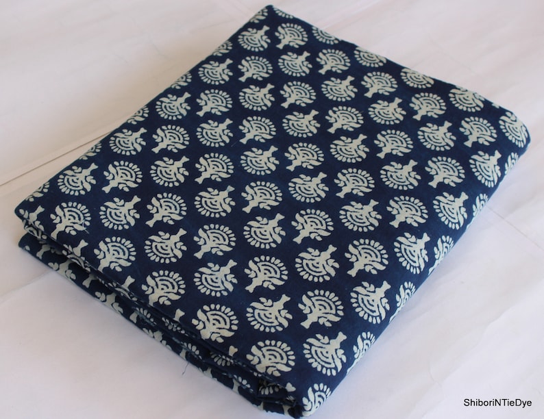 May include: A folded piece of blue cotton fabric with a white floral pattern. The fabric is folded in thirds and has a white background with a blue floral pattern.