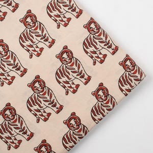 May include: Cream-colored fabric with a repeating pattern of stylized tigers in shades of red and brown. The tigers are depicted in a seated position with detailed stripes, creating a playful and artistic design. This fabric is suitable for various craft projects.