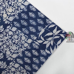 May include: A section of indigo blue fabric with white floral and leaf patterns. The fabric is divided into sections with different designs, including large floral motifs and smaller, repeating leaf shapes. The fabric is likely used for textiles or crafts.