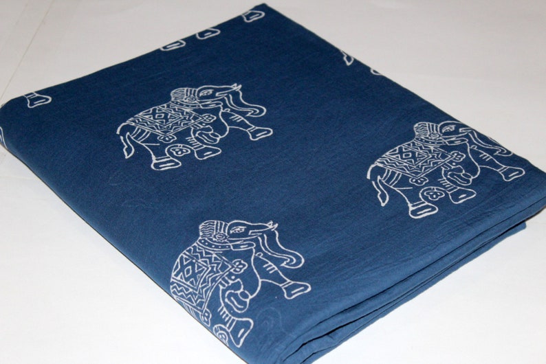 May include: A folded blue cotton fabric with a white elephant print. The fabric is folded in thirds and has a blue background with white elephants printed on it.