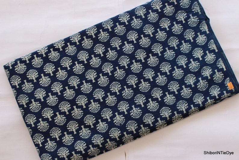 May include: A blue cotton fabric with a white floral pattern. The fabric is folded in half and has a small brown tag with the text "ShiboriNTieDye" on it.