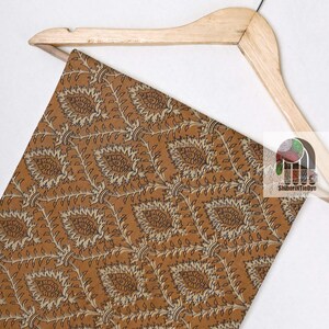 May include: A brown fabric with a beige and black floral pattern. The fabric is draped over a wooden hanger.