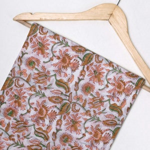 May include: A white fabric with a floral pattern in shades of orange, brown, and green. The fabric is draped over a wooden hanger.