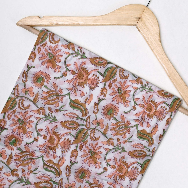 May include: A white fabric with a floral pattern in shades of orange, brown, and green. The fabric is draped over a wooden hanger.