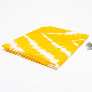 May include: Yellow fabric with a white tie-dye pattern. The fabric is folded in half and the edges are visible.