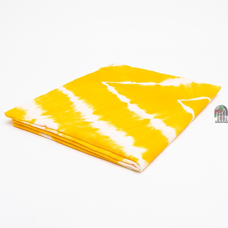 May include: Yellow fabric with a white tie-dye pattern. The fabric is folded in half and the edges are visible.