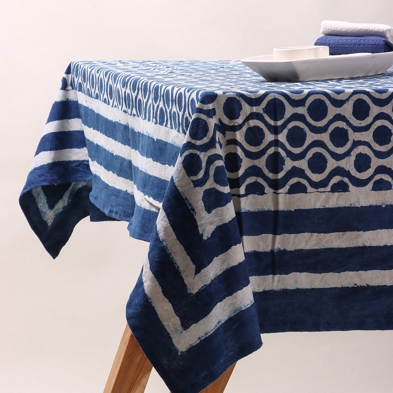 May include: A blue and white cotton tablecloth with a geometric pattern. The tablecloth has a striped border and a central design of circles and wavy lines.