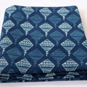 May include: A blue cotton fabric with a white patterned design of kites. The fabric is folded in thirds.