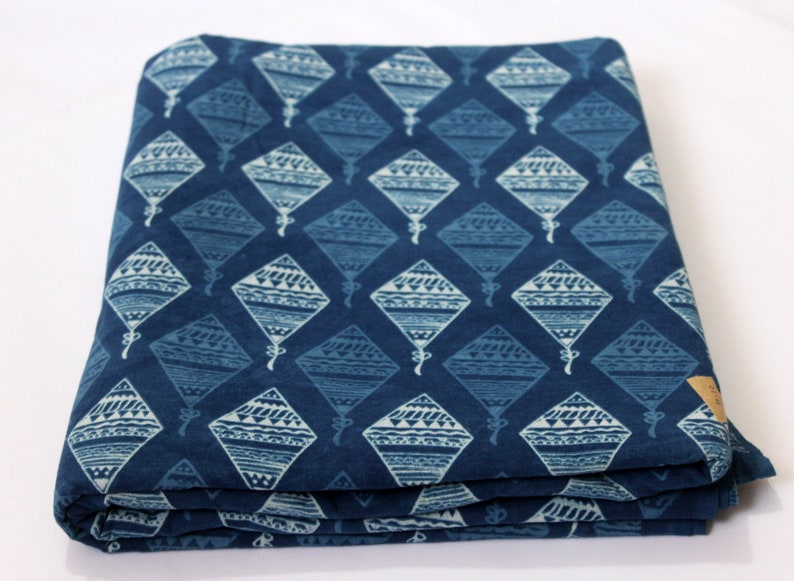 May include: A blue cotton fabric with a white patterned design of kites. The fabric is folded in thirds.