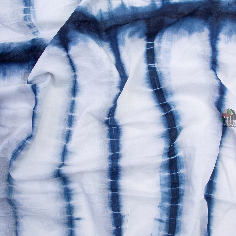 Op de afbeelding: Witte stof met blauwe tie-dye strepen. De stof is gevouwen en gekreukt.