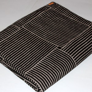 May include: Folded fabric with a black and off-white striped pattern. The stripes are arranged in a geometric design, creating a block-like appearance. The fabric is neatly folded, showcasing the pattern's repeating design.