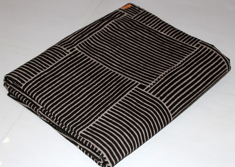 May include: Folded fabric with a black and off-white striped pattern. The stripes are arranged in a geometric design, creating a block-like appearance. The fabric is neatly folded, showcasing the pattern's repeating design.
