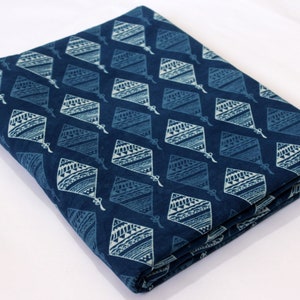 May include: A folded piece of blue cotton fabric with a white geometric pattern. The fabric is printed with a repeating pattern of diamond shapes with intricate designs.