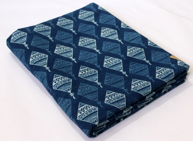 May include: A folded piece of blue cotton fabric with a white geometric pattern. The fabric is printed with a repeating pattern of diamond shapes with intricate designs.