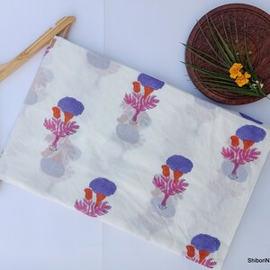 Puede incluir: Tela blanca con un estampado floral repetido en morado, naranja y rosa. La tela est&aacute; doblada y colocada sobre una percha de madera. Un plato de madera con flores y vegetaci&oacute;n est&aacute; en el fondo.