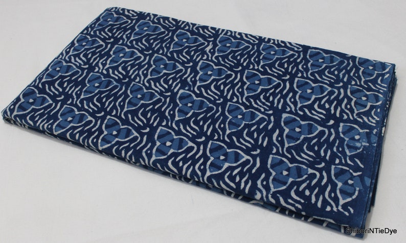 May include: A folded piece of blue and white fabric with a geometric pattern. The fabric is made of cotton and has a soft, natural feel.