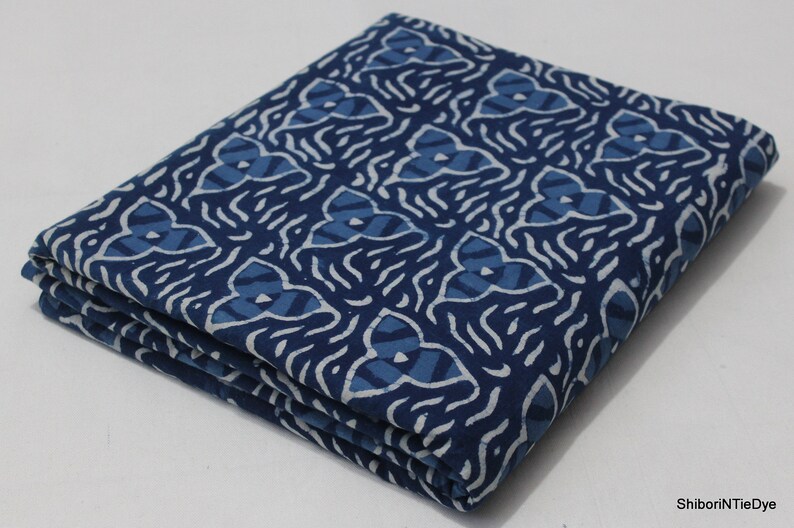 May include: A folded blue and white cotton fabric with a geometric pattern. The fabric is folded in thirds and has a white background with a blue pattern.