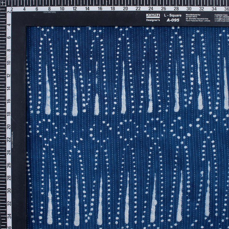 May include: A blue fabric with a white pattern of dots and vertical lines. The fabric has a textured surface and is made of cotton. The fabric is labelled "KHYATI Designer's L-Square A-095".