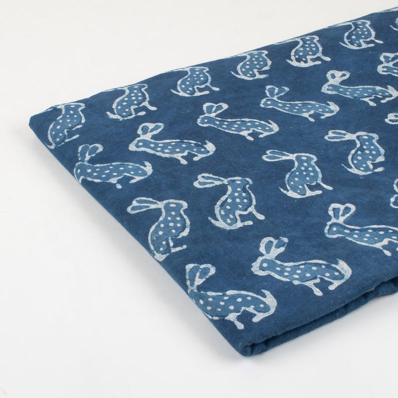 May include: A folded piece of indigo blue fabric with a repeating pattern of white rabbits. The rabbits are stylized with dotted bodies and long ears. The fabric is likely cotton or linen.