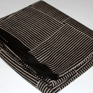 May include: Folded black and beige fabric with a striped pattern. The fabric is arranged in a rectangular shape, with the stripes forming a grid-like design. The fabric appears to be soft and pliable, suitable for various textile projects.