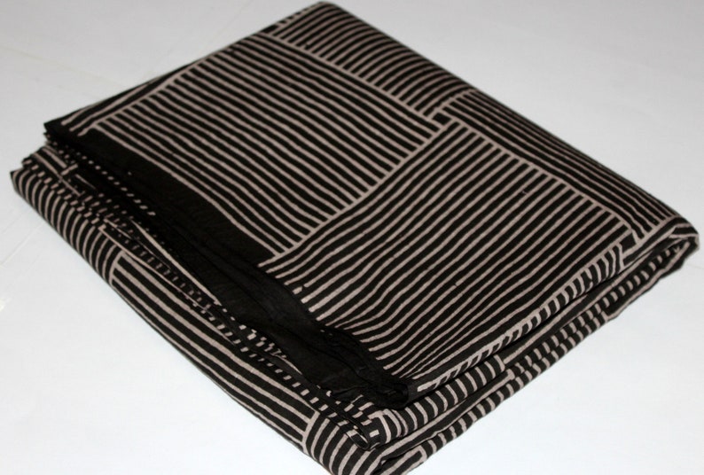 May include: Folded black and beige fabric with a striped pattern. The fabric is arranged in a rectangular shape, with the stripes forming a grid-like design. The fabric appears to be soft and pliable, suitable for various textile projects.