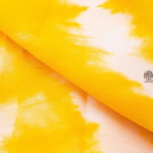 May include: Yellow fabric with a white tie-dye pattern. The fabric is folded in half, showing the texture of the material.