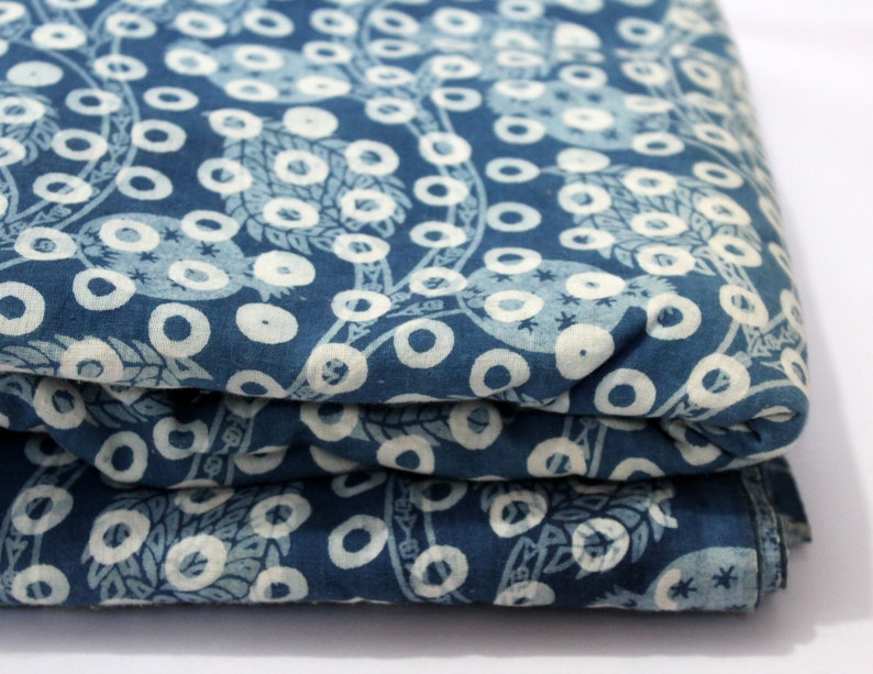 May include: A folded piece of blue fabric with a white pattern of circles and leaves. The fabric is a cotton blend and has a soft, natural feel.