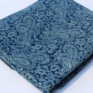 May include: A folded piece of blue fabric with a white paisley pattern. The fabric is folded in thirds and has a small brown tag with the text "ShiboriNTieDye" on it.