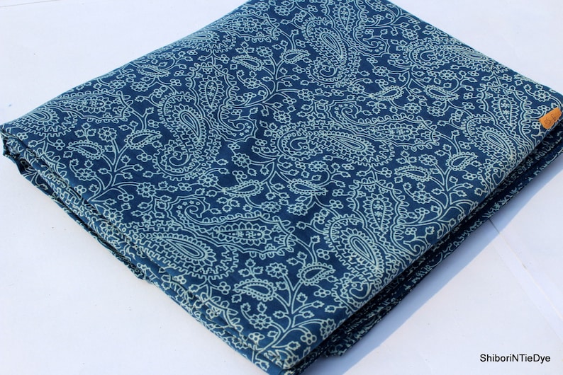 May include: A folded piece of blue fabric with a white paisley pattern. The fabric is folded in thirds and has a small brown tag with the text "ShiboriNTieDye" on it.