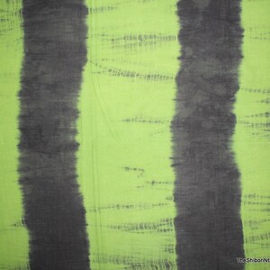 Op de afbeelding: Groen stof met twee verticale zwarte strepen. De stof heeft een tie-dye patroon met een lichtgroene achtergrond en donkergroene strepen.