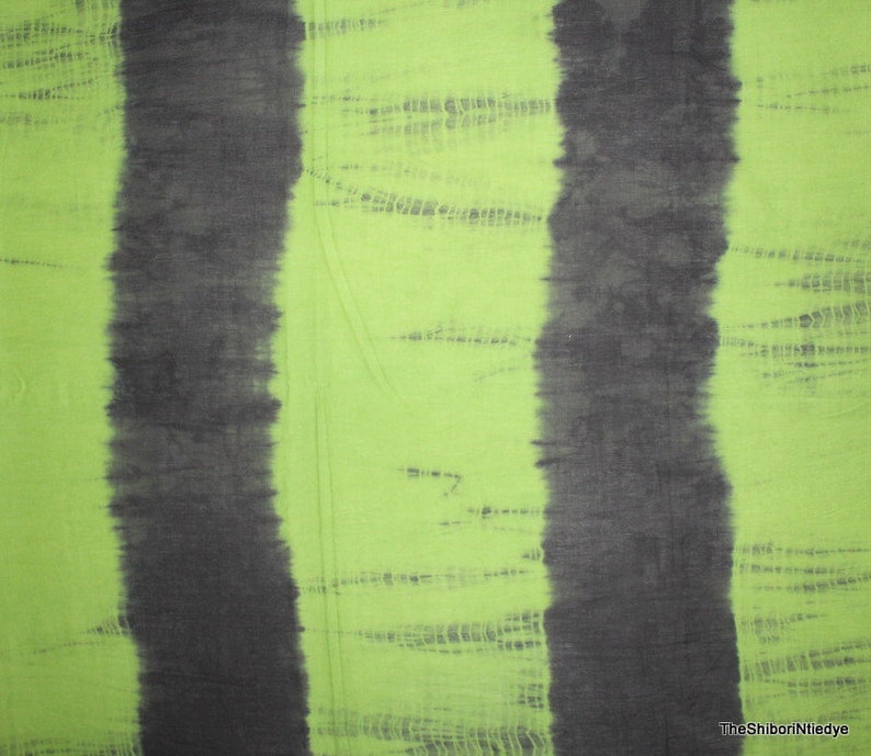 Op de afbeelding: Groen stof met twee verticale zwarte strepen. De stof heeft een tie-dye patroon met een lichtgroene achtergrond en donkergroene strepen.