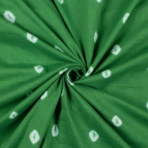 May include: Green fabric with white tie-dye dots. The fabric is folded and twisted, showing the texture of the material.