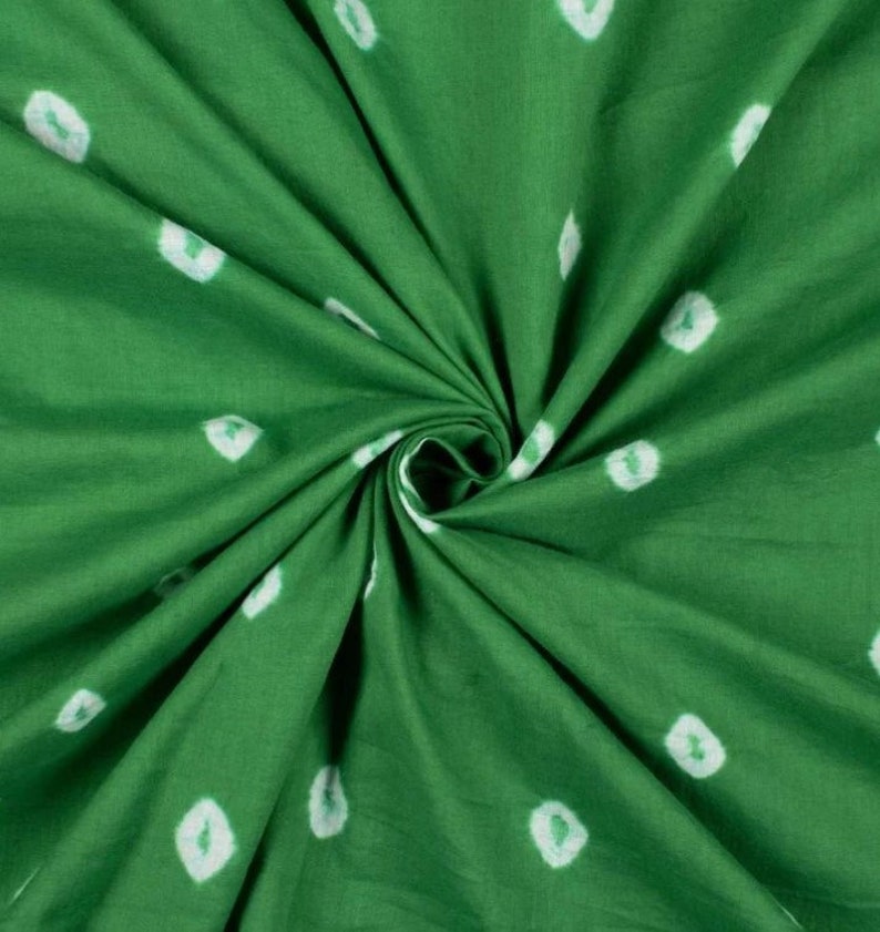 May include: Green fabric with white tie-dye dots. The fabric is folded and twisted, showing the texture of the material.