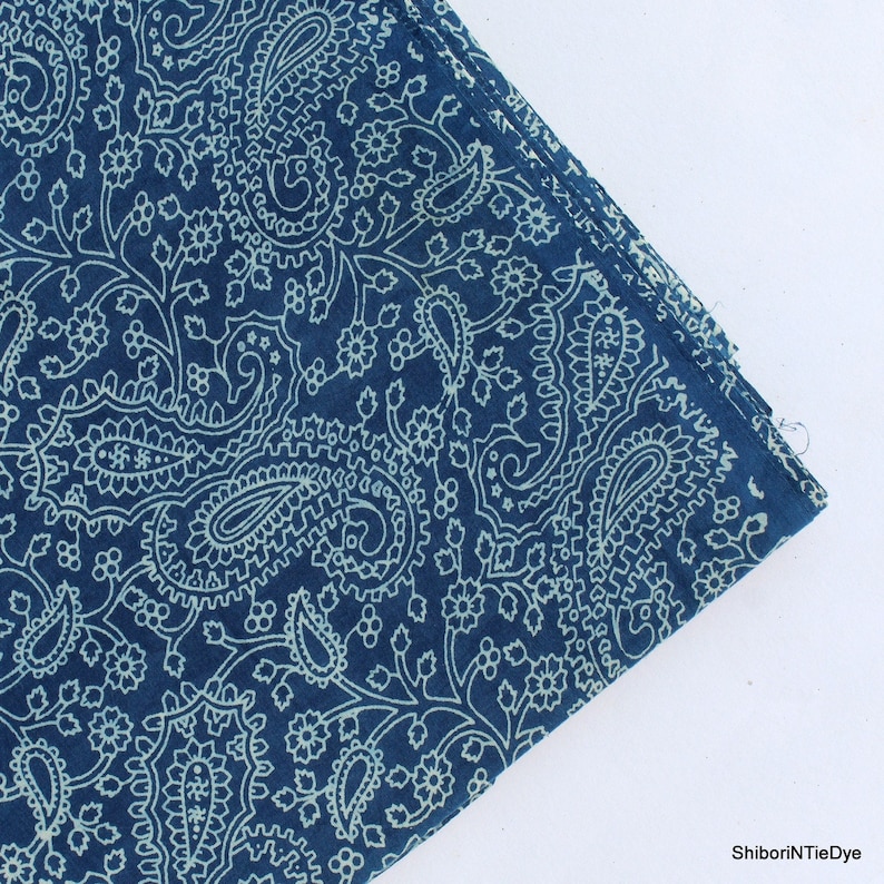 May include: A blue cotton fabric with a white paisley pattern. The fabric is folded in the upper right corner.