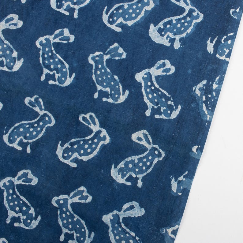 May include: A dark blue fabric with a repeating pattern of white rabbits. The rabbits are stylized with long ears and dotted bodies. The fabric has a slightly textured appearance, with the white pattern contrasting against the deep blue background.