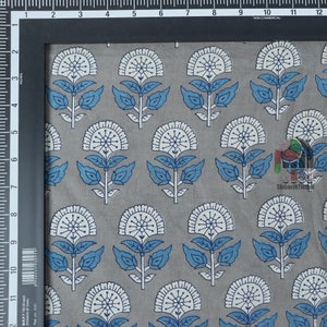 Pu&ograve; includere: Primo piano di un tessuto di cotone grigio con un motivo floreale bianco e blu. Il tessuto &egrave; stampato con un motivo ripetitivo di fiori stilizzati con foglie blu e centri bianchi.
