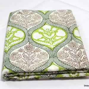 May include: A folded piece of white fabric with a green and brown floral print. The fabric has a repeating pattern of teardrop shapes with a floral design inside.