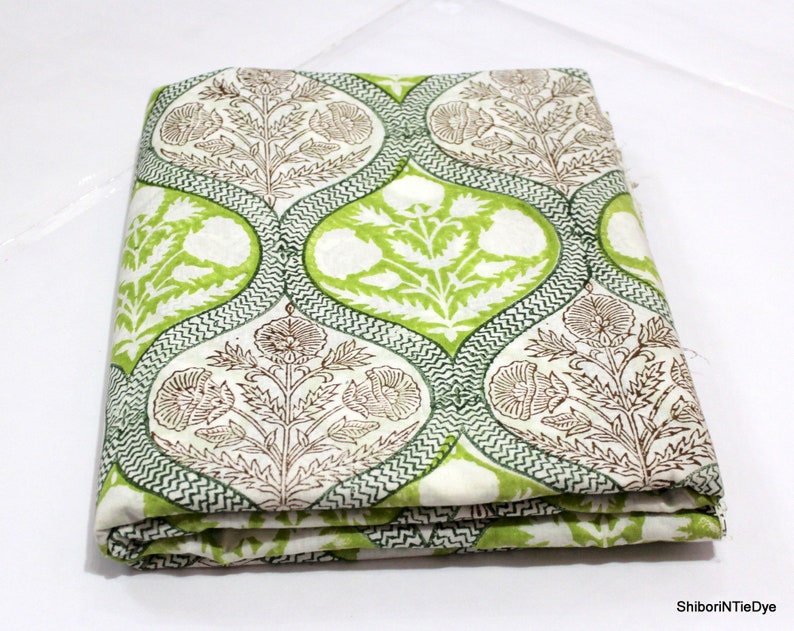 May include: A folded piece of white fabric with a green and brown floral print. The fabric has a repeating pattern of teardrop shapes with a floral design inside.