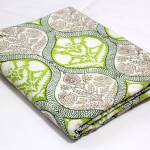 May include: A white cotton fabric with a green and brown floral print. The fabric is folded in thirds and has a repeating pattern of stylised flowers and leaves.