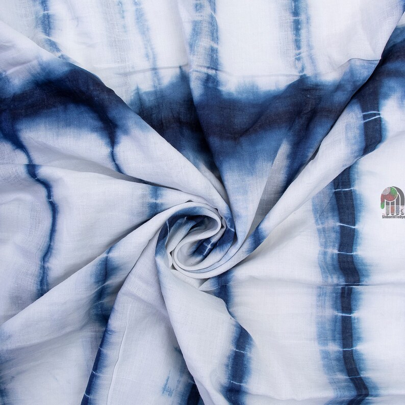Op de afbeelding: Witte stof met een blauw tie-dye patroon. De stof is gevouwen en gedraaid, waardoor het patroon in detail zichtbaar is.