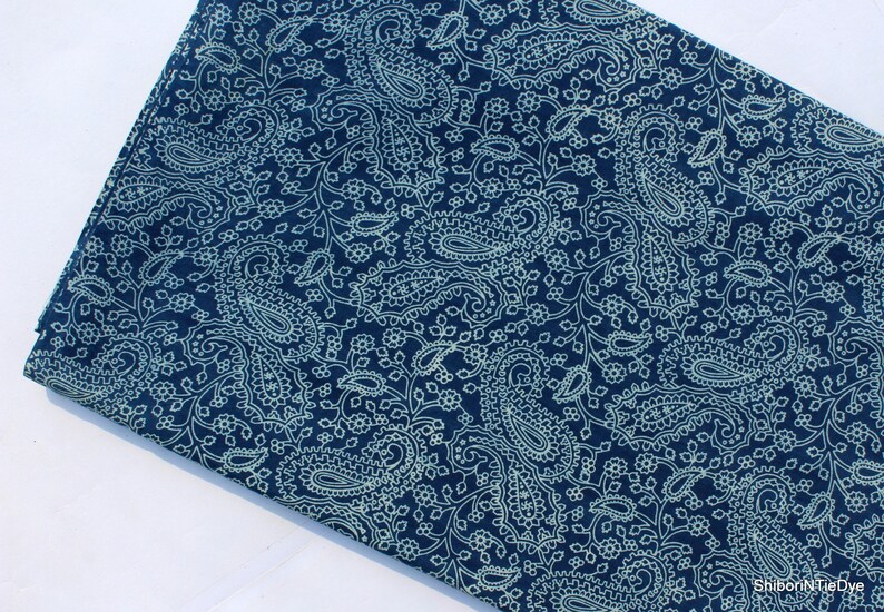 May include: A dark blue fabric with a white paisley pattern. The fabric is soft and has a smooth texture.