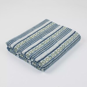 May include: Folded fabric with a striped pattern in shades of blue and white, accented with rows of small green floral designs. The fabric is neatly stacked, suggesting it's ready for use in sewing or crafting projects.