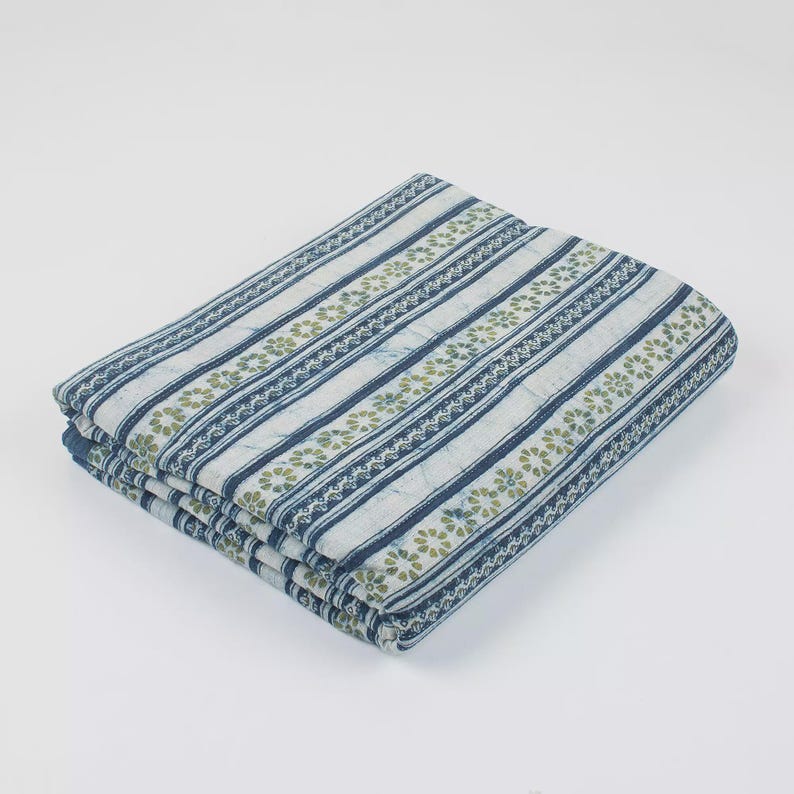 May include: Folded fabric with a striped pattern in shades of blue and white, accented with rows of small green floral designs. The fabric is neatly stacked, suggesting it's ready for use in sewing or crafting projects.