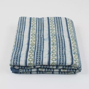 May include: Folded blue and white patterned fabric. The fabric features vertical stripes with a floral design in green. The stripes alternate between solid blue and white with a blue floral pattern. The fabric is folded neatly.