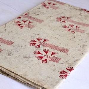 May include: A white fabric with a red tree pattern. The fabric is folded in half and has a subtle speckled texture.